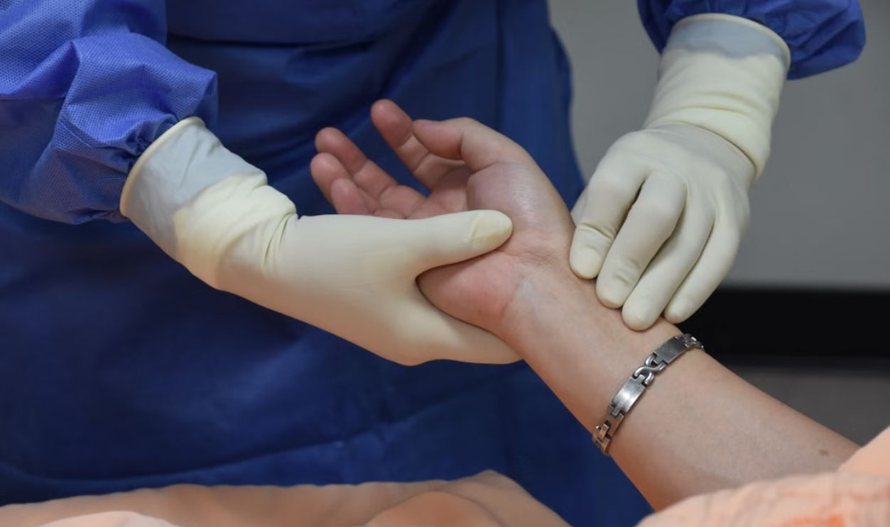A medical professional wearing PPE checks a patient's pulse indoors