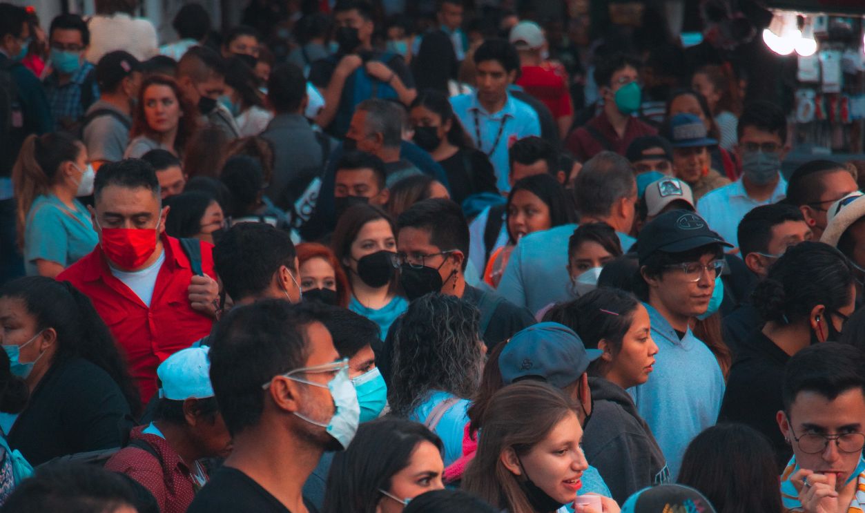 A diverse crowd wearing face masks gathered in a busy urban street, showcasing cultural diversity