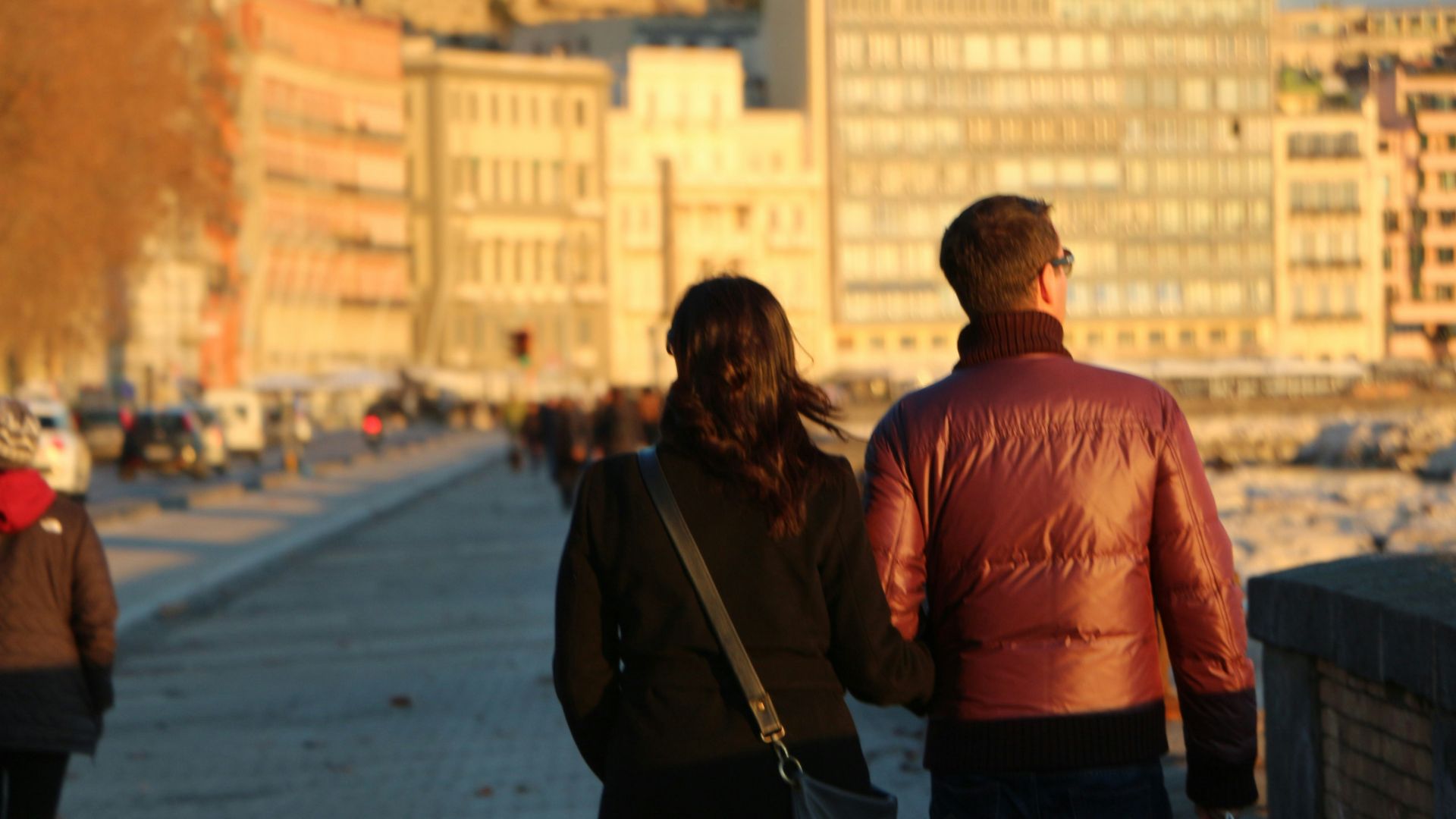 Couple walking along a waterfront with buildings.