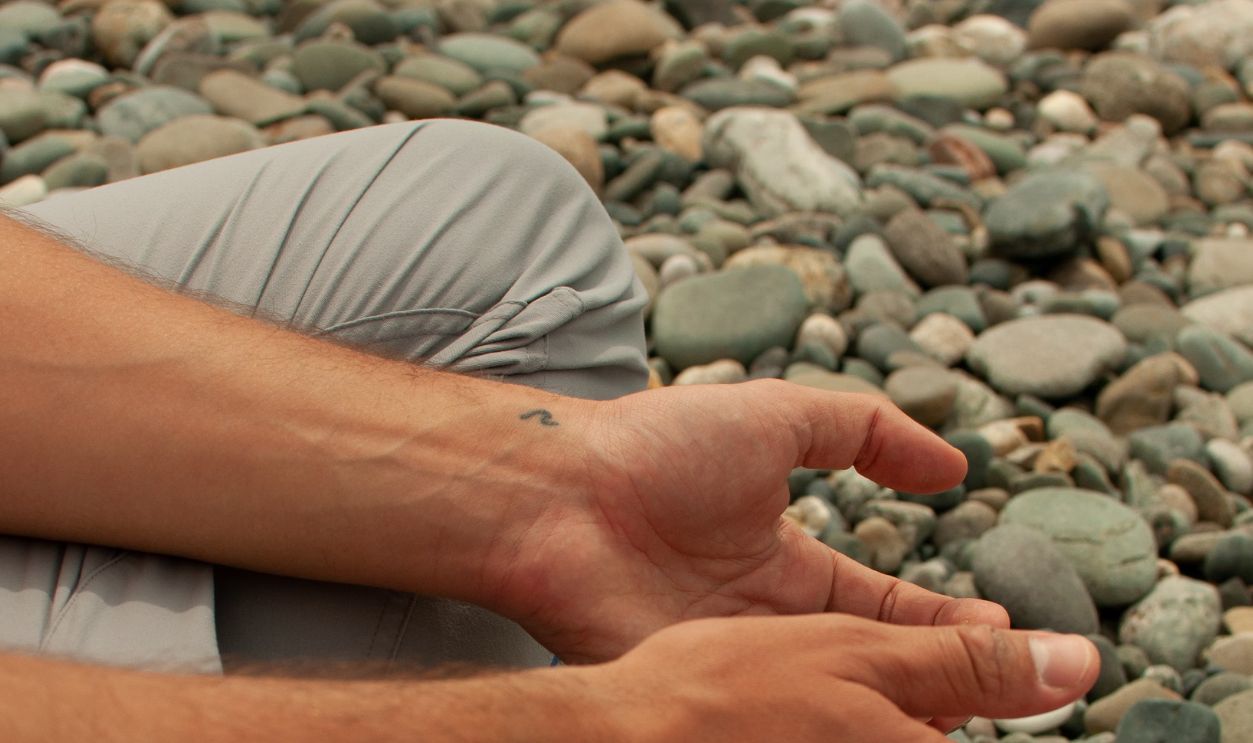 Close-up of hands in a meditative pose while sitting on a pebble beach