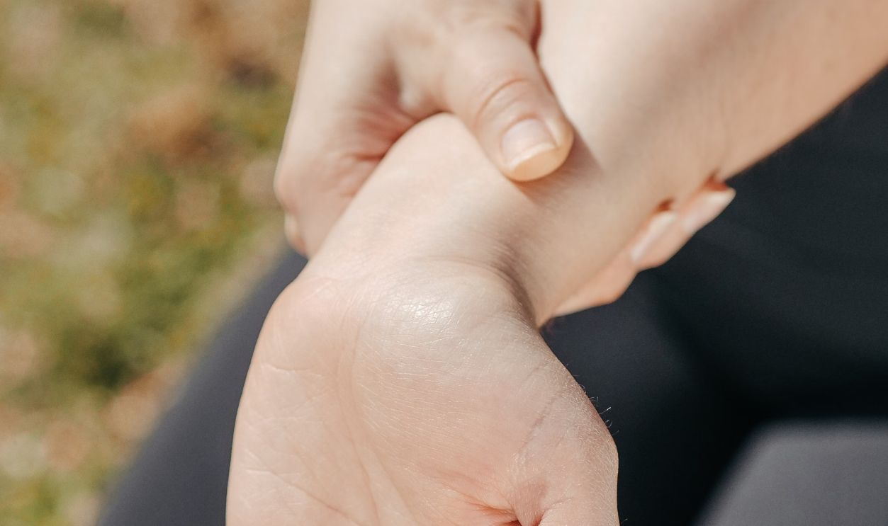 Close-up of a woman's hand holding her wrist outdoors, symbolizing injury or pain relief