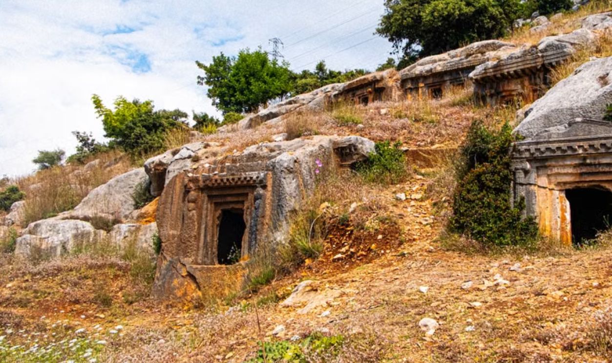 Explore ancient rock-cut tombs nestled in a scenic hillside landscape, captured brilliantly under a clear sky
