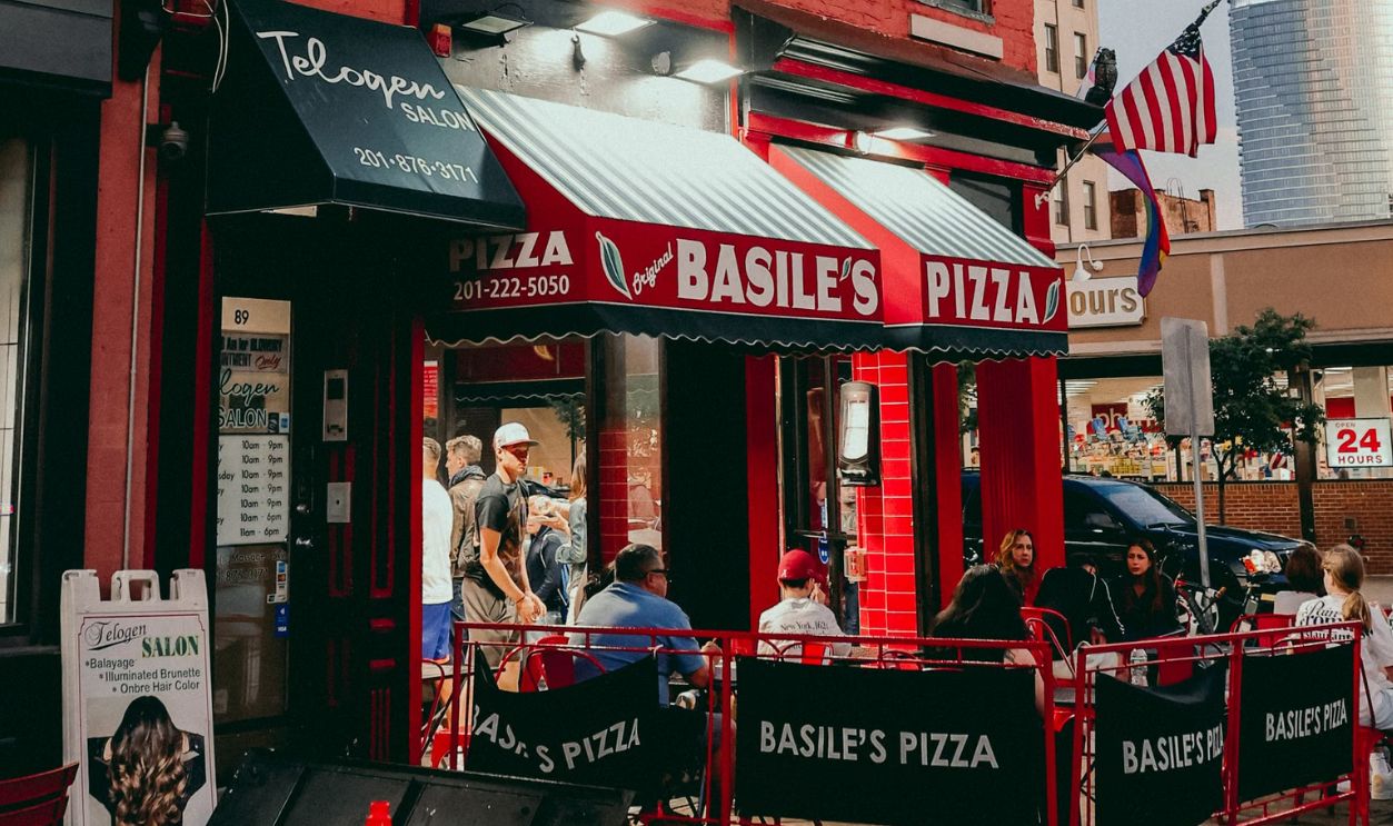 Outdoor seating at Basile's Pizza in Hoboken, NJ on a sunny day. Iconic red-brick building