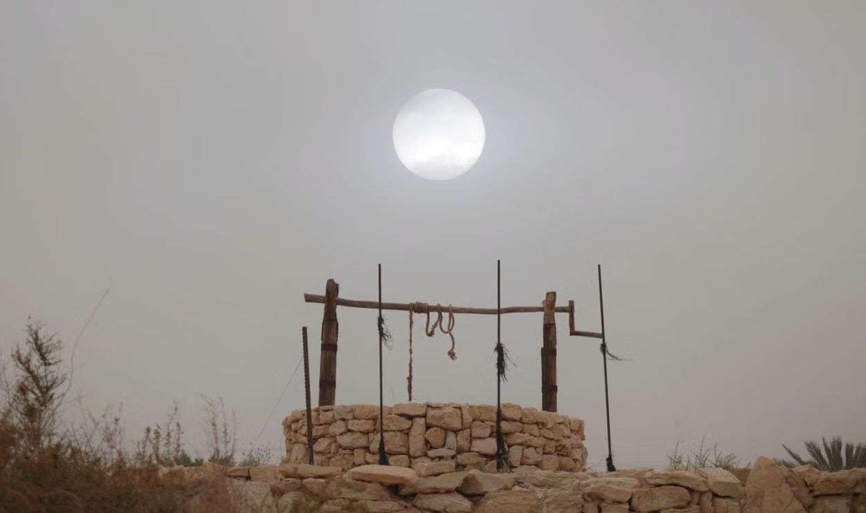 A rustic stone well under a foggy sky with the sun visible, capturing a serene rural scene