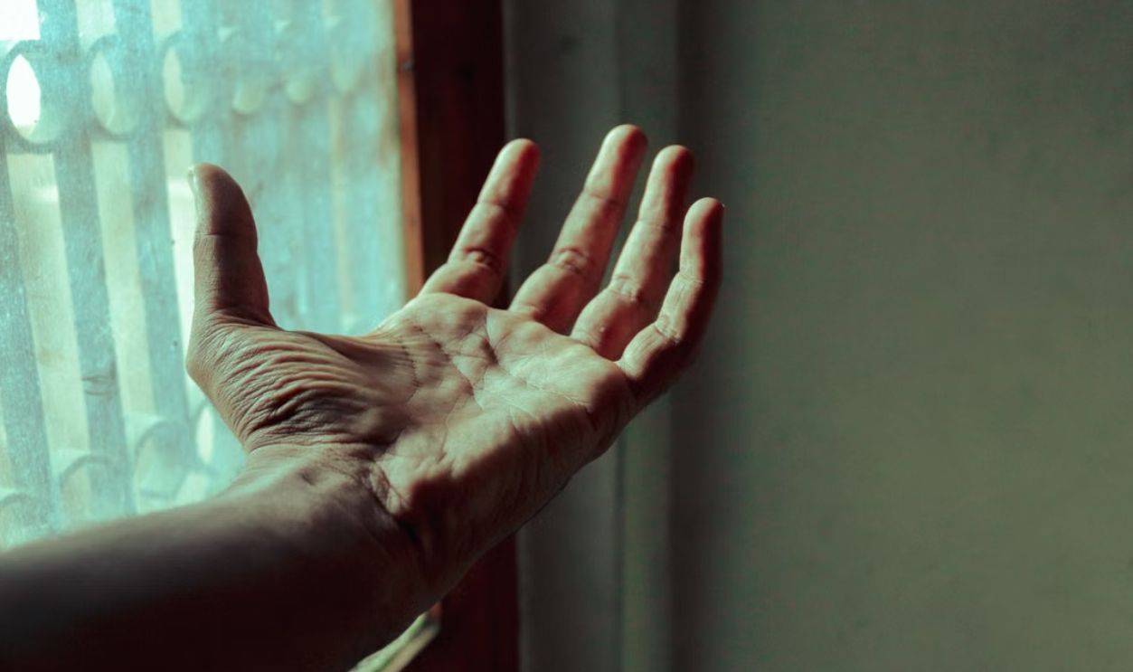 Close-up of a hand reaching out towards a window, illuminated by soft light