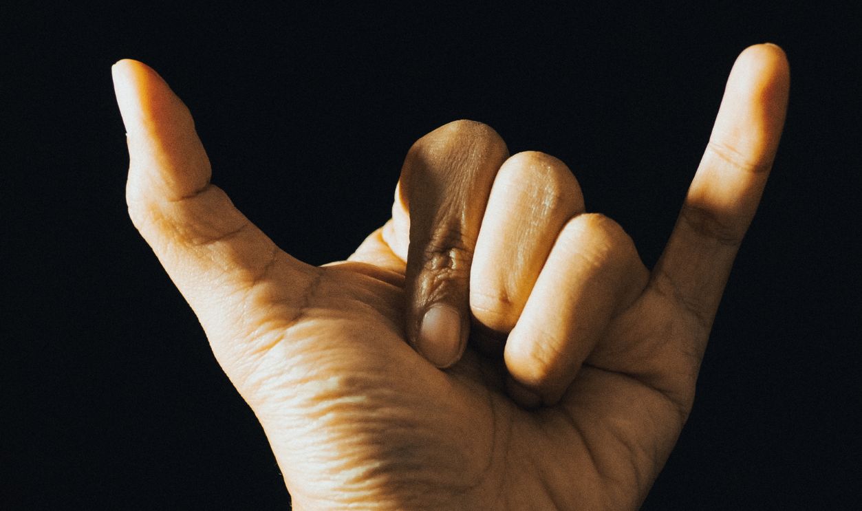 a male left hand with thumb and little finger pointing up isolated in a black background