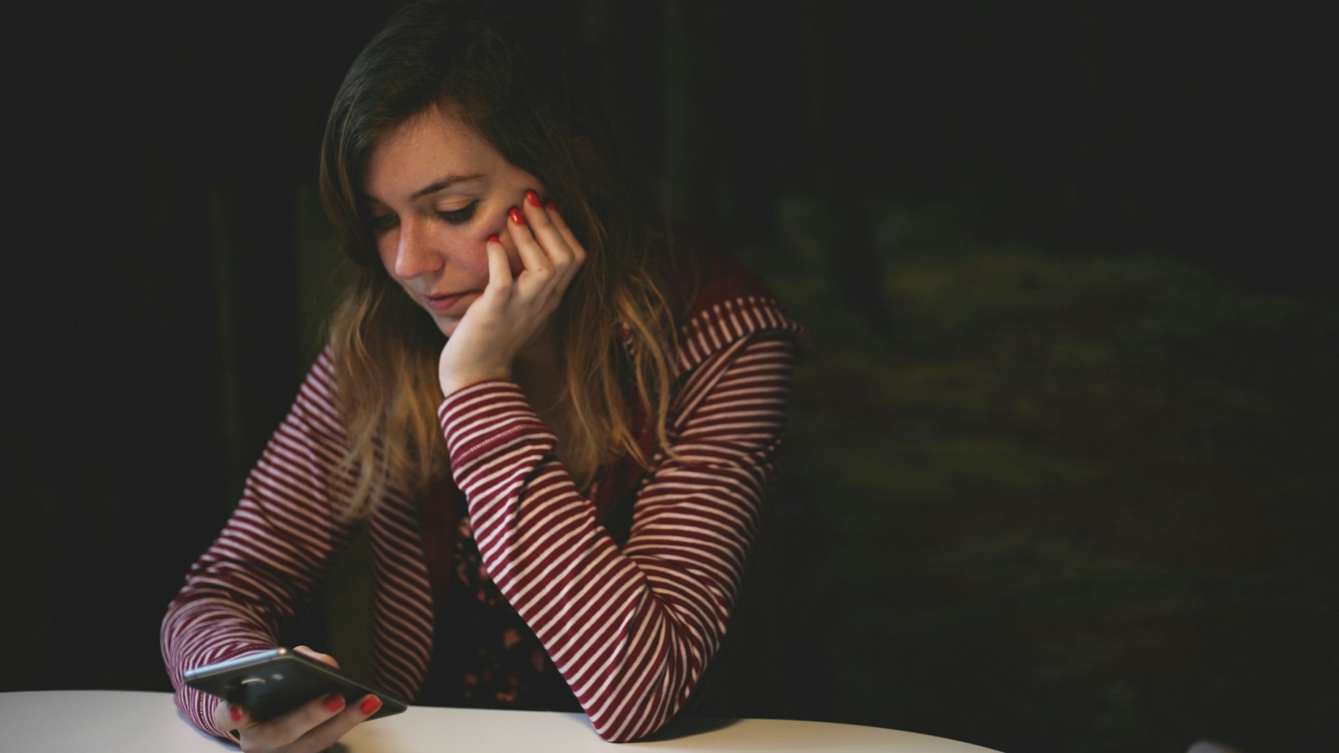 woman leaning on white wooden table while holding black Android smartphone
