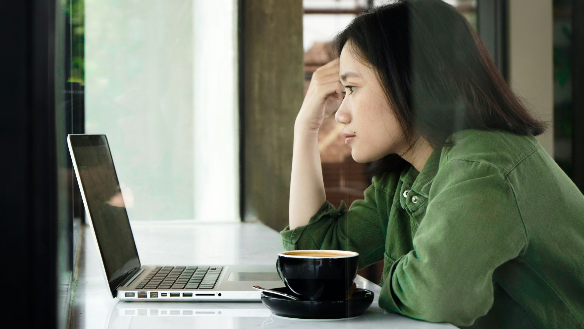 woman in green jacket sitting by the table using laptop