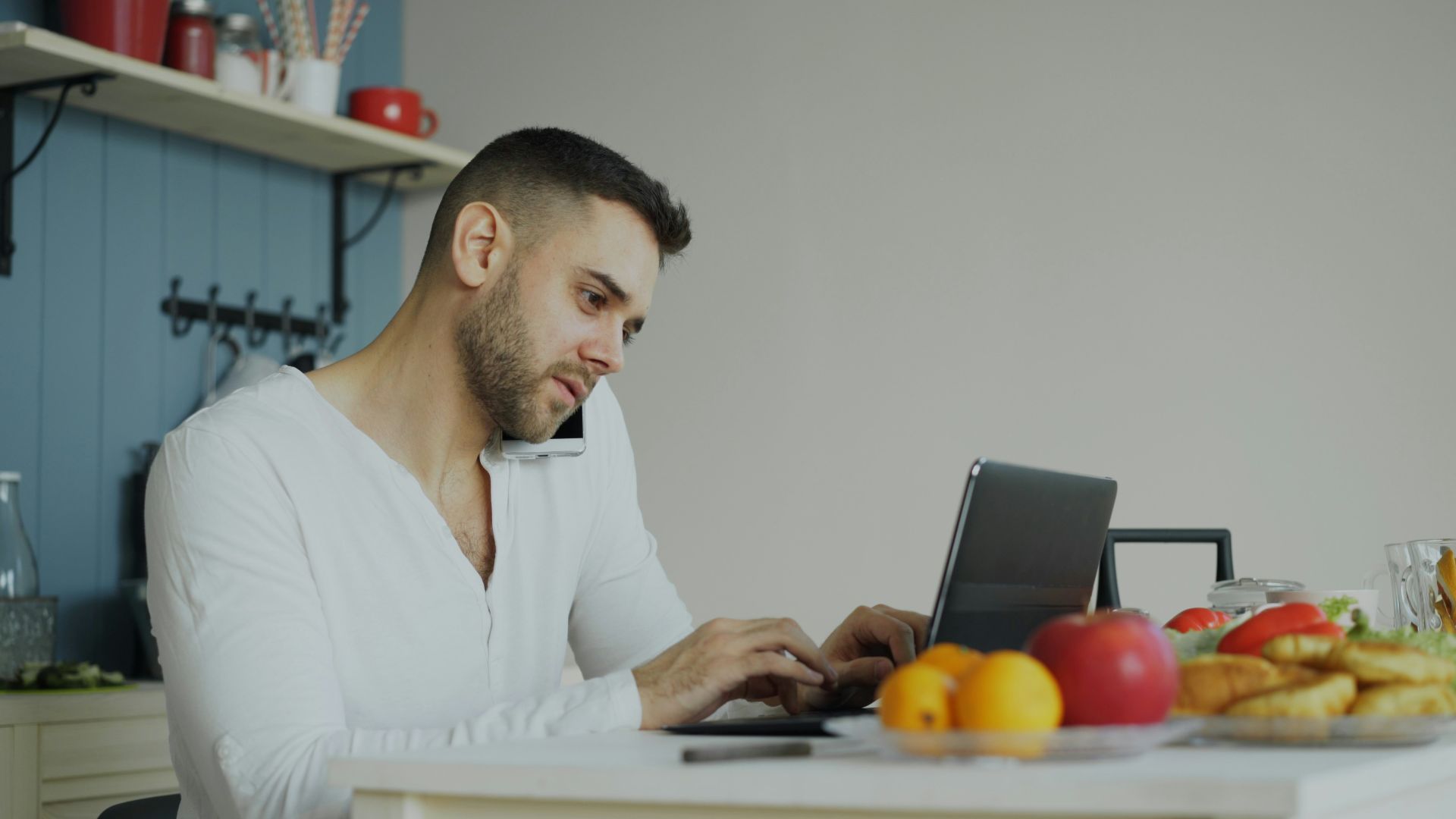 Man on phone and laptop at kitchen table