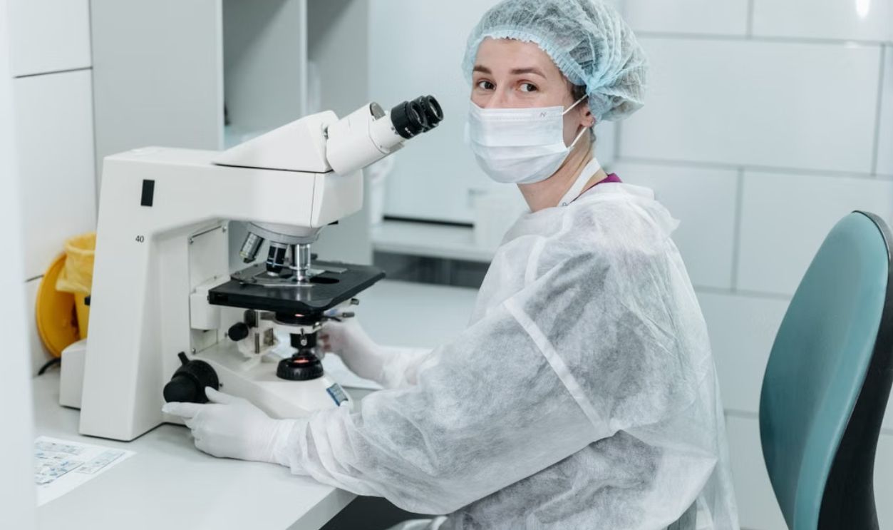 Scientist working with microscope in sterile lab environment, wearing protective gear and a mask