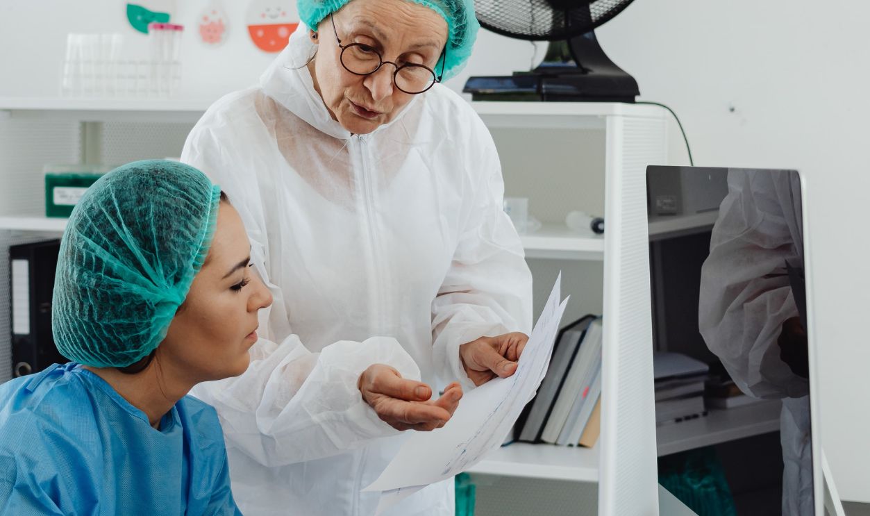 Two medical professionals in protective gear discuss research on a tablet in a laboratory setting