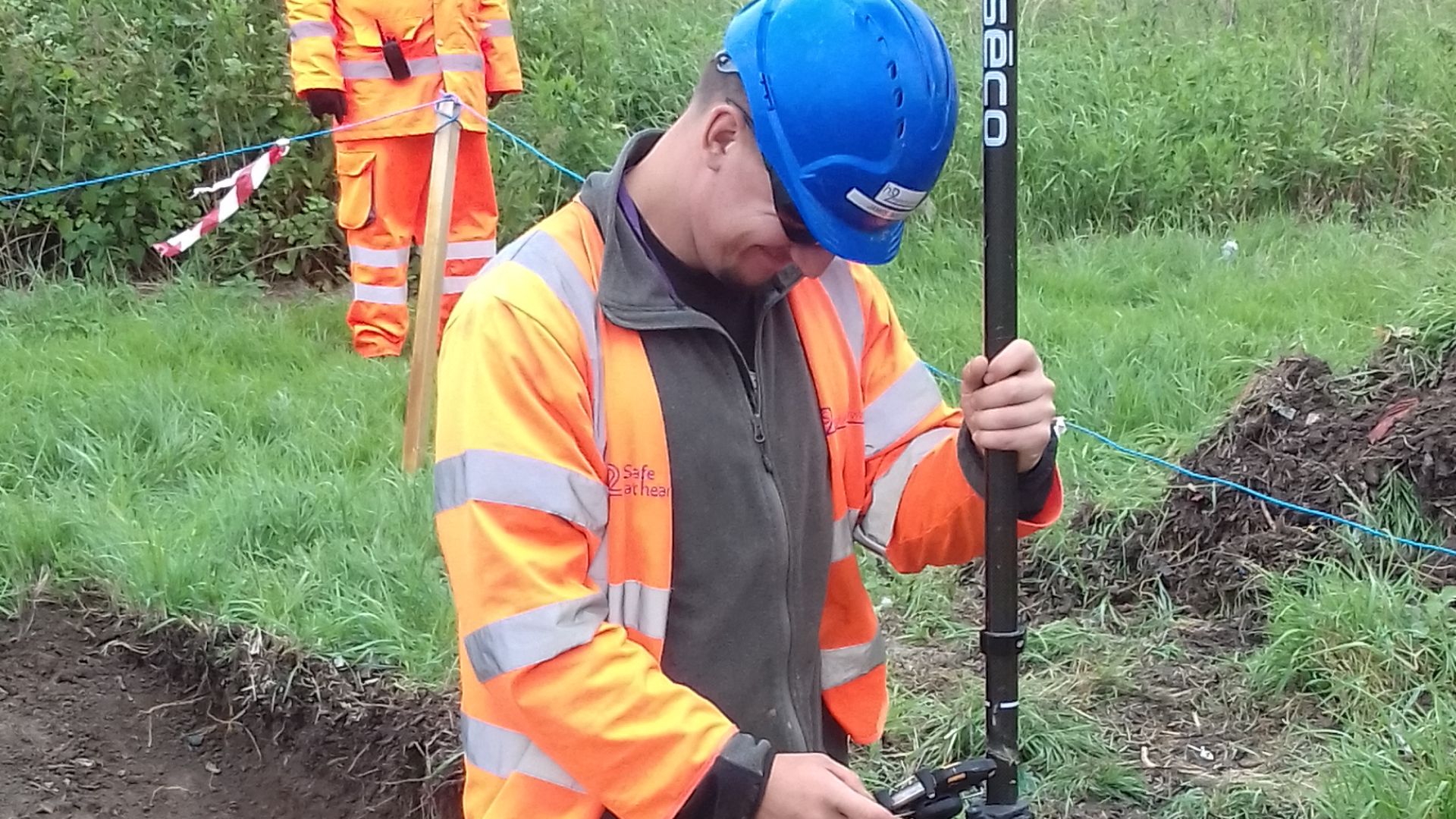 An archaeologist standing in a trench holding a GPS unit.