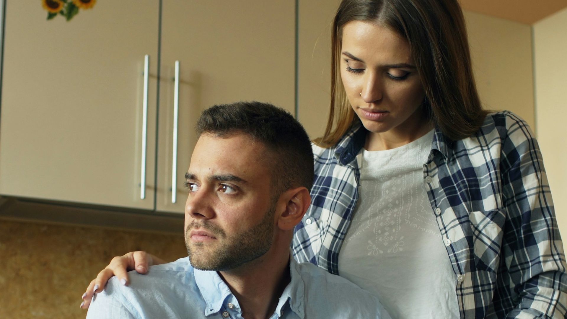Woman comforts man at kitchen table with food.