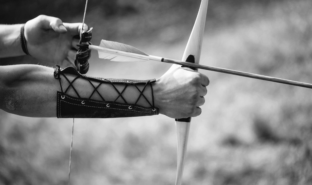 Archer hands with bow shoot arrow with blue and yellow fletchings on natural background