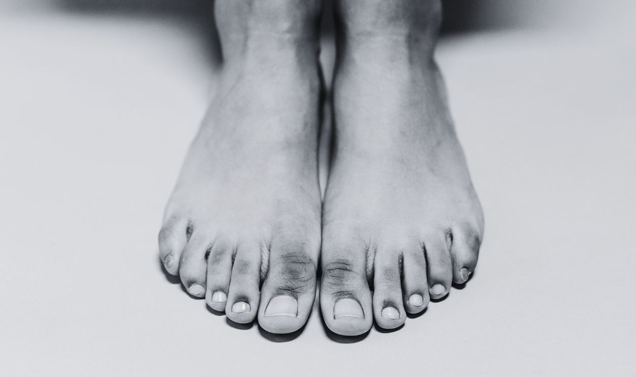 Intimate close-up of a person's bare feet and legs sitting on a studio floor in a minimalistic setting