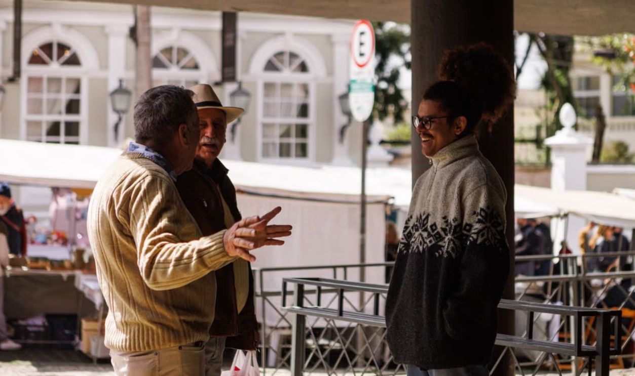 Three men casually chatting in an outdoor market in Curitiba, Brazil, captured during a sunny day.