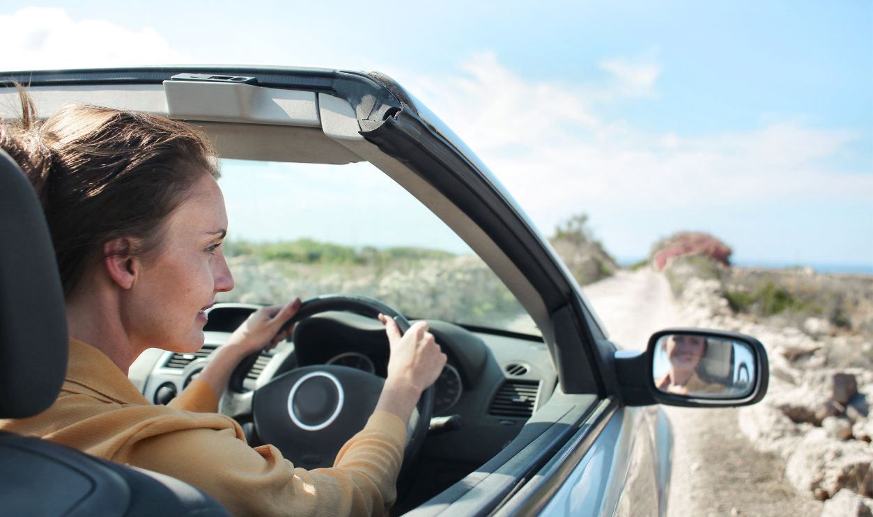 A woman drives a convertible on a sunny day