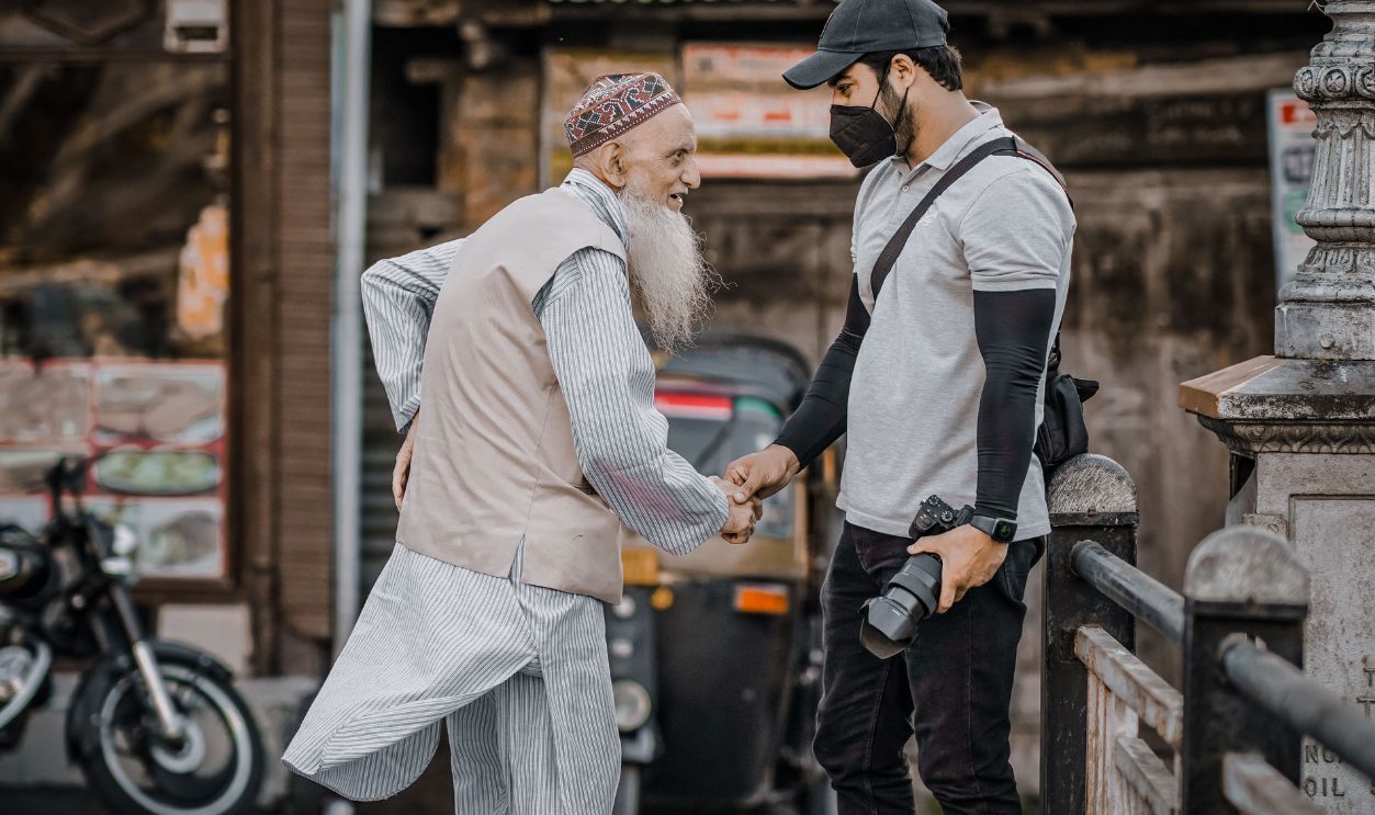 Elderly man and photographer shake hands on a busy street, capturing a moment of connection