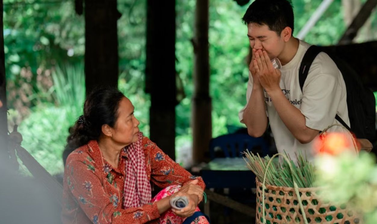 A warm interaction between two people in an outdoor market setting, surrounded by greenery