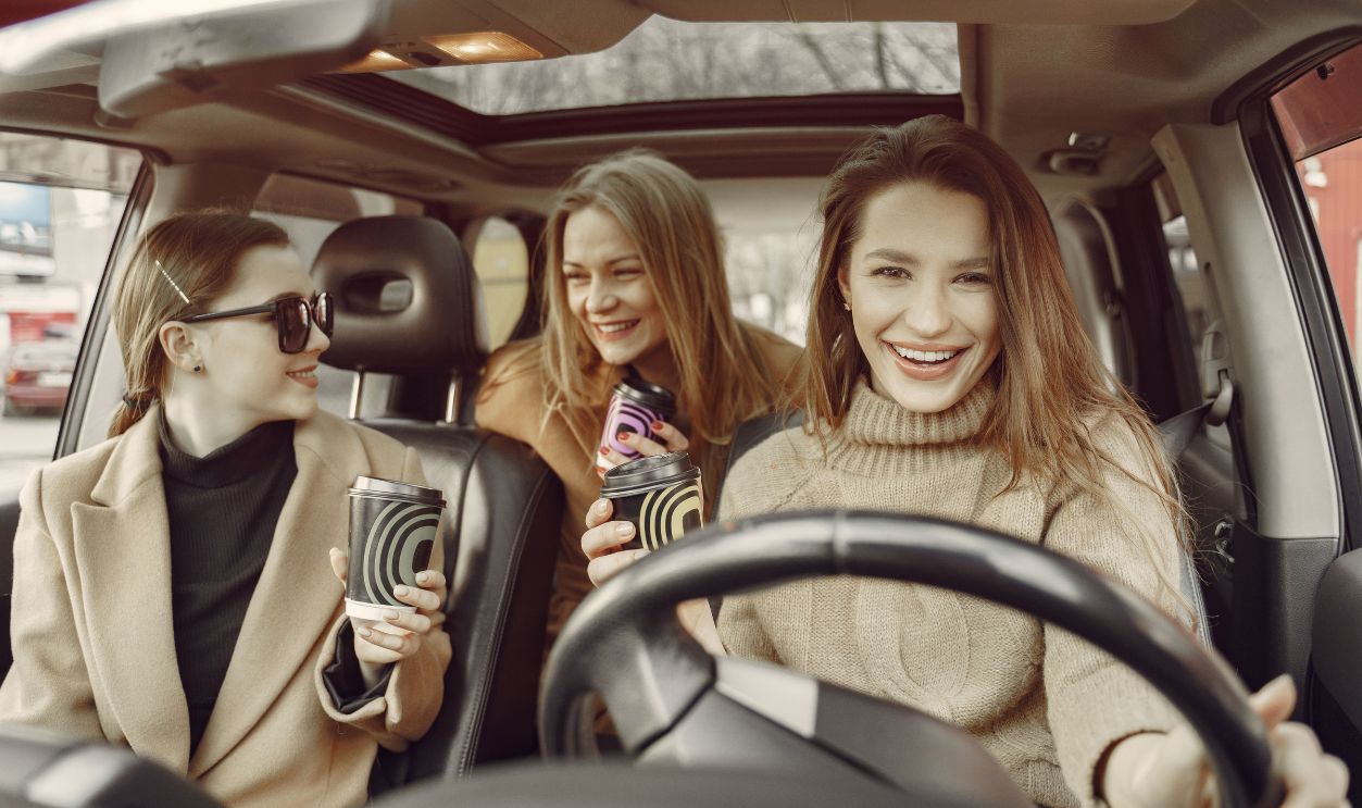 Happy friends relaxing with takeaway coffee in a car, sharing laughter and enjoyment