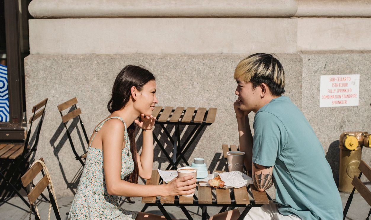 Young couple enjoying a sunny morning coffee date outdoors, smiling and talking