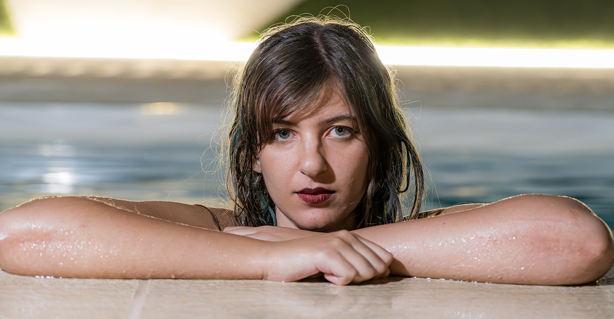 Young woman with wet hair leaning at the side of a pool.