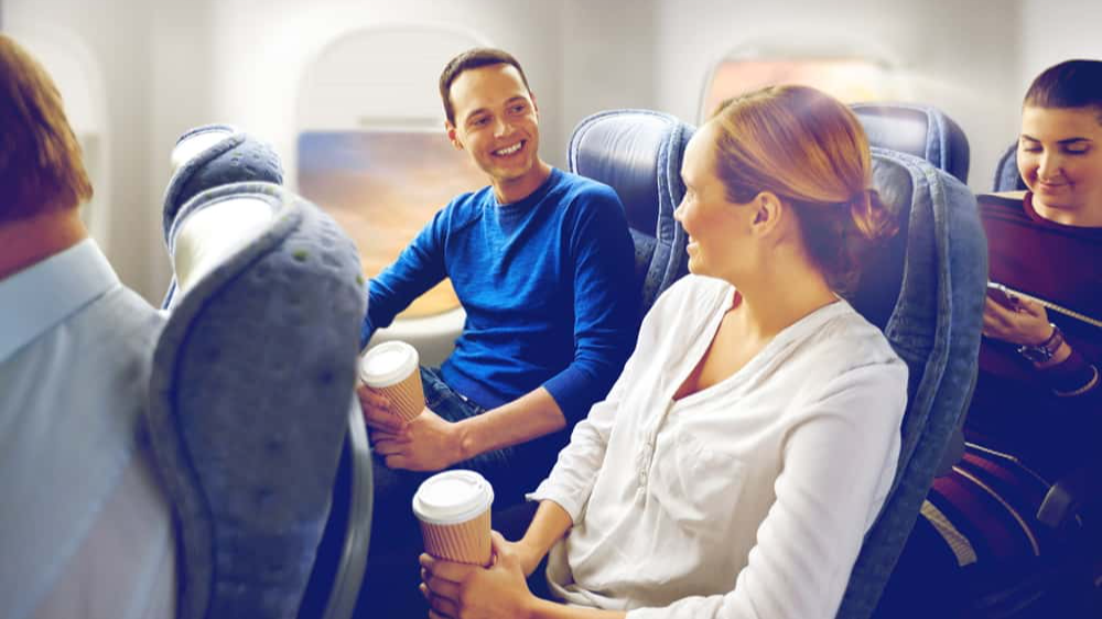 transport, tourism and air flights concept - happy passengers or tourists with coffee talking in plane over porthole background