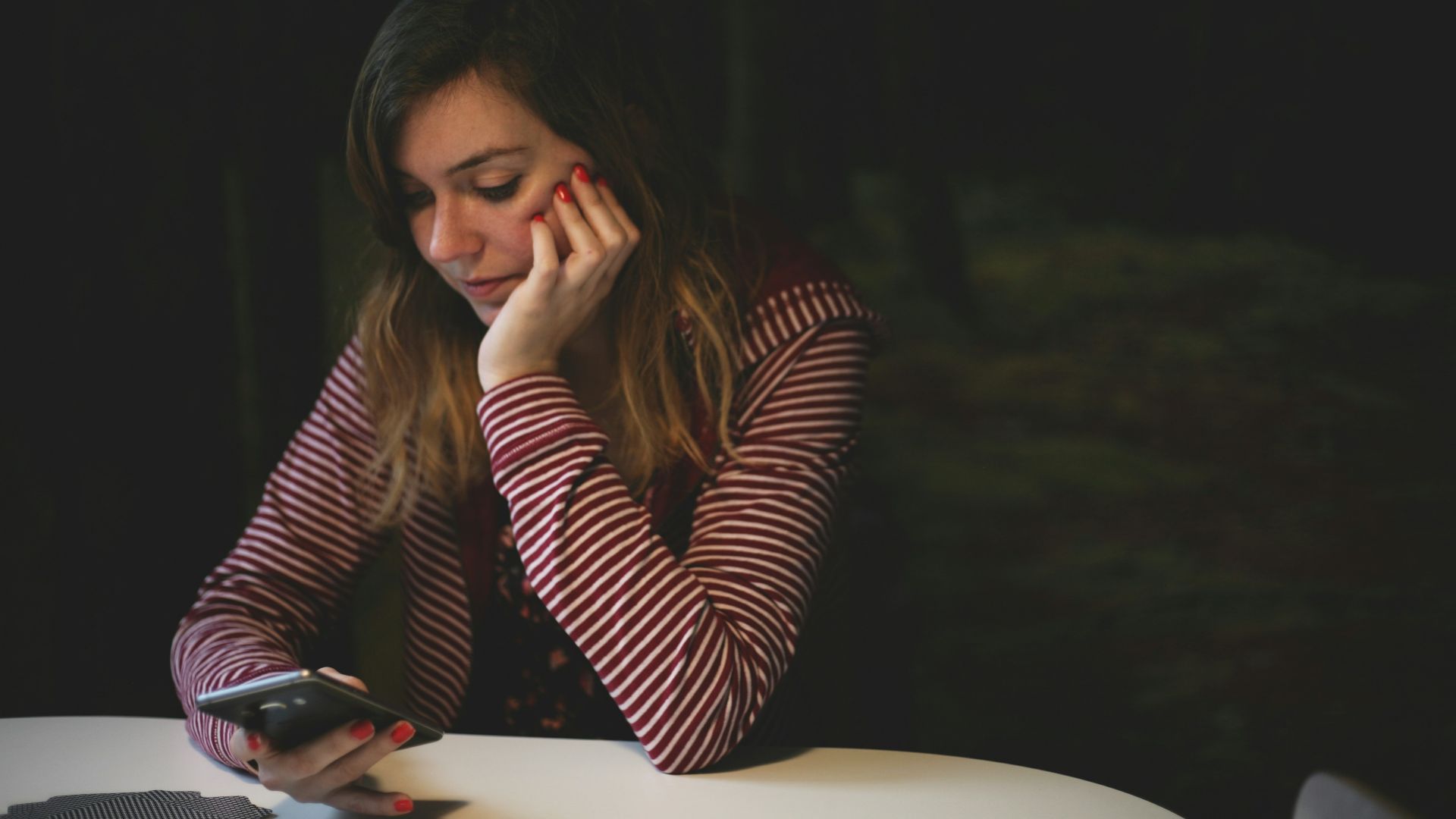 woman leaning on white wooden table while holding black Android smartphone