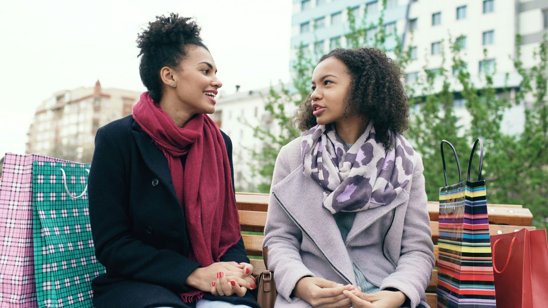 Two women sitting on a bench with shopping bags.