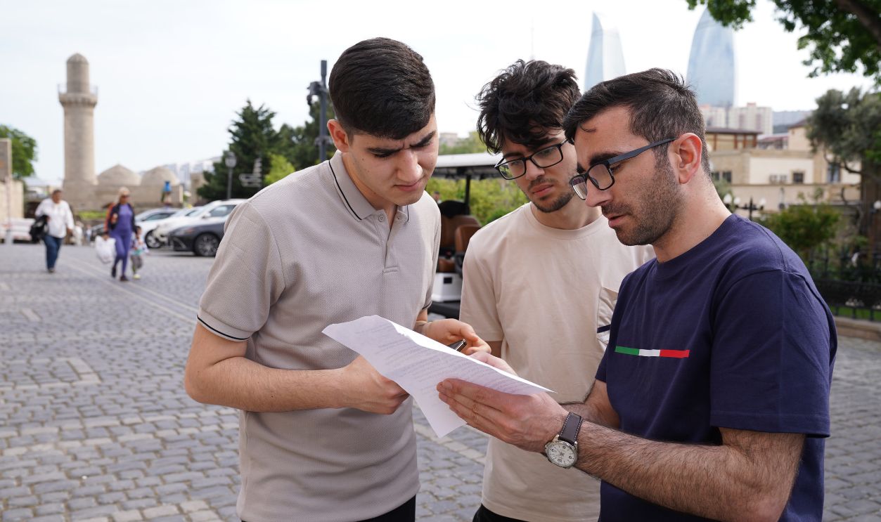Three men discussing papers in Baku's old city with iconic Flame Towers in the background