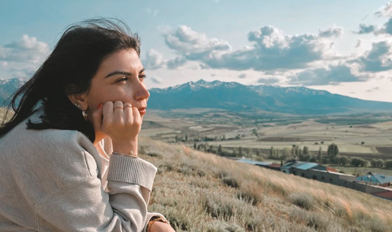 Young woman gazing thoughtfully at scenic mountains under a blue sky