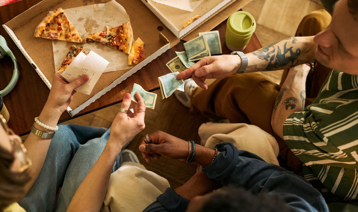 Overhead view of multiethnic young adults splitting cash and checking receipt over shared pizza, showing group expense sharing and casual budgeting. Useful for payment apps or cost sharing ads