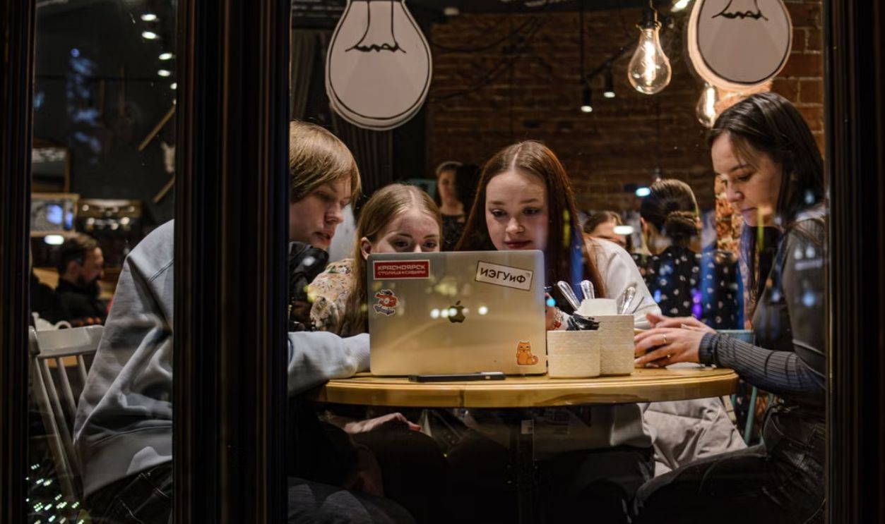 Four friends collaborating on a laptop inside a cozy cafe, reflecting modern lifestyle