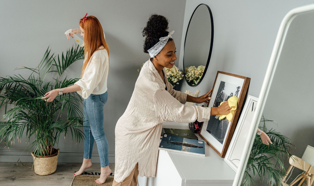 Two women joyfully clean a home interior with plant