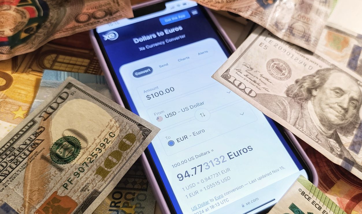 A smartphone displaying a currency converter surrounded by dollar and euro banknotes, highlighting exchange rates