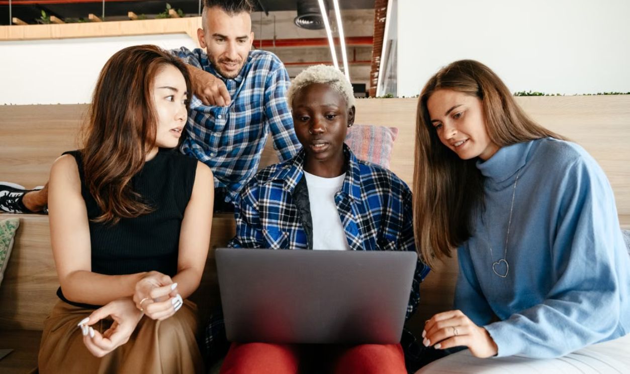 A diverse group of young professionals engaged in a collaborative project using a laptop in a modern office setting