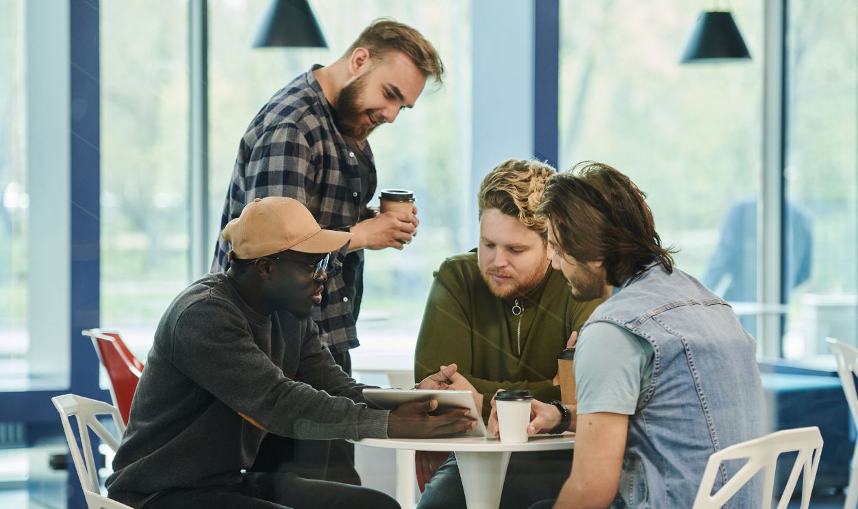 Four men having a collaborative meeting at a cafe, engaging with digital technology