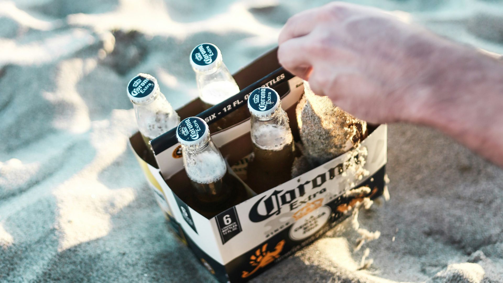 Hand reaching for six-pack of corona beer on sand