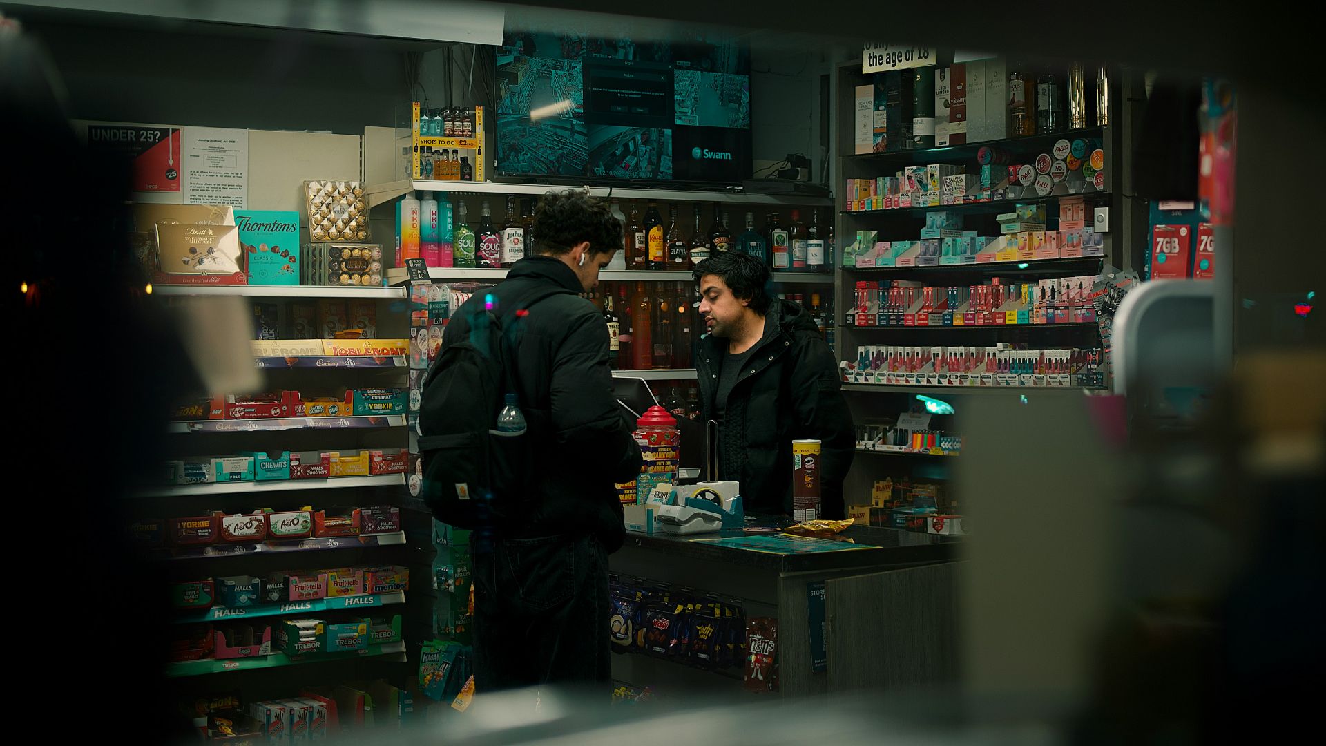 Two men talking inside a brightly lit convenience store.