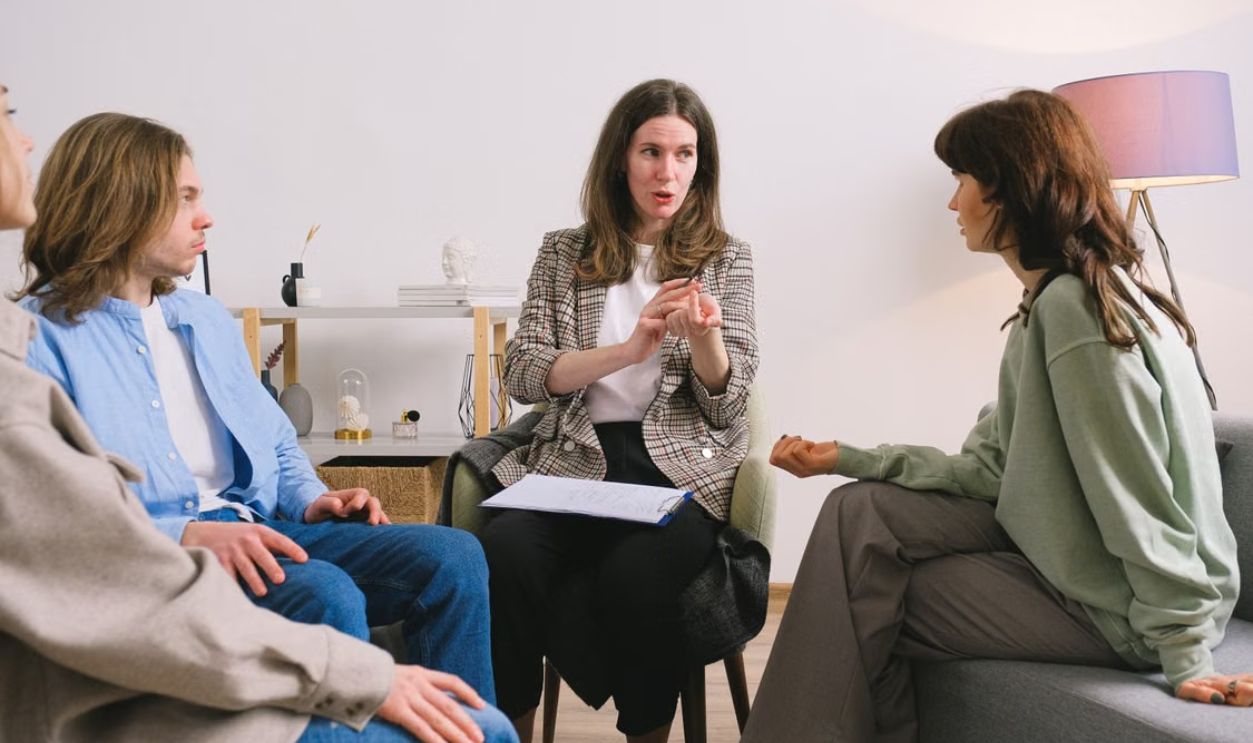 Four adults engaged in a group therapy session inside a well-lit room.