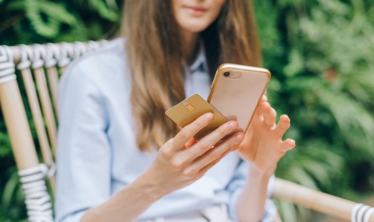 A woman making an online purchase using a smartphone and credit card outdoors.