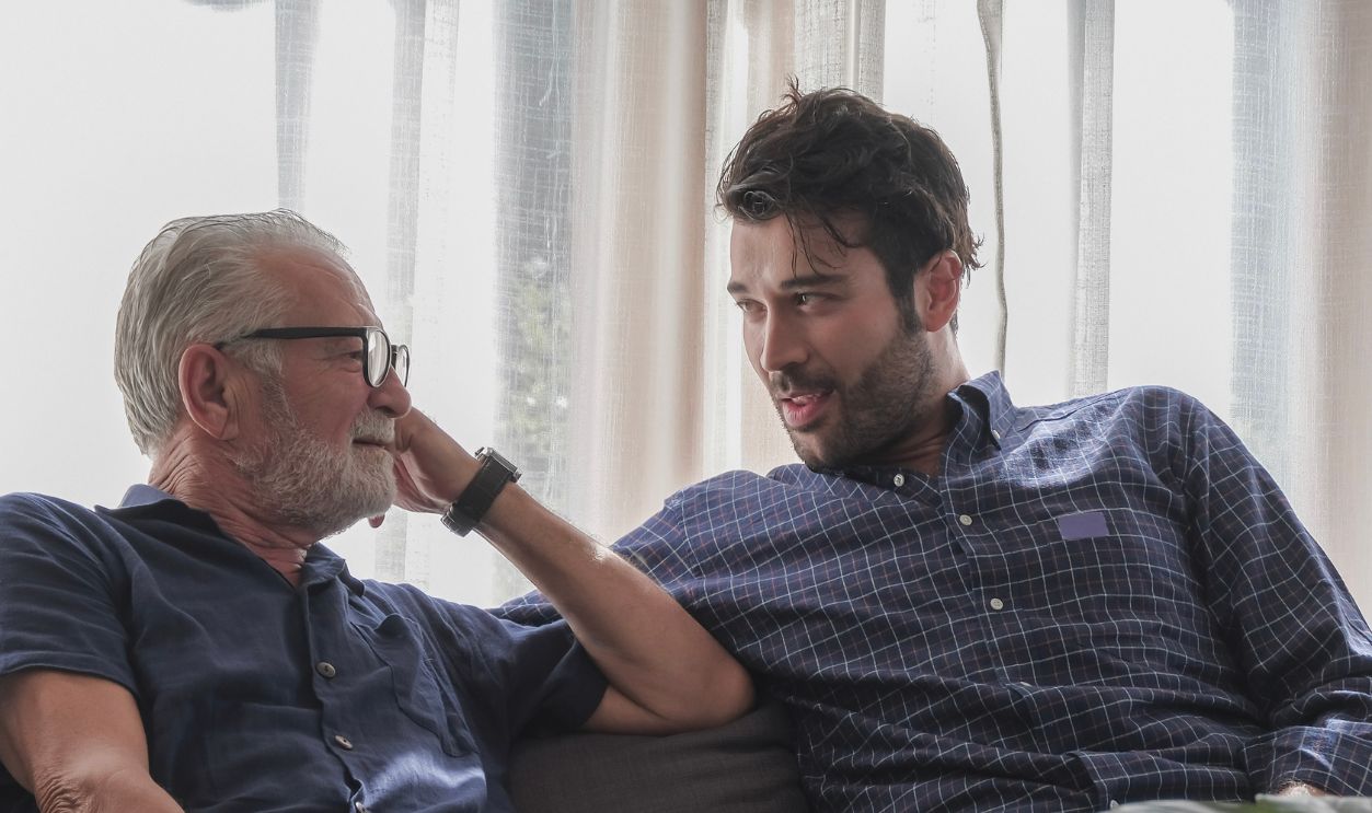 Sharing family story and authentic lifestyle concept. Two of dad and his son are relax talking in happy moment at cozy living room warmth house during holiday with coffee cup on the desk.