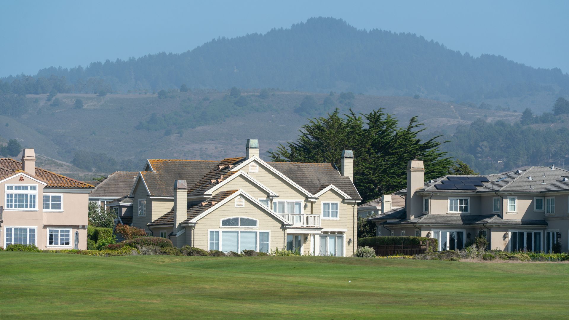 Suburban houses on a green lawn with hills behind.