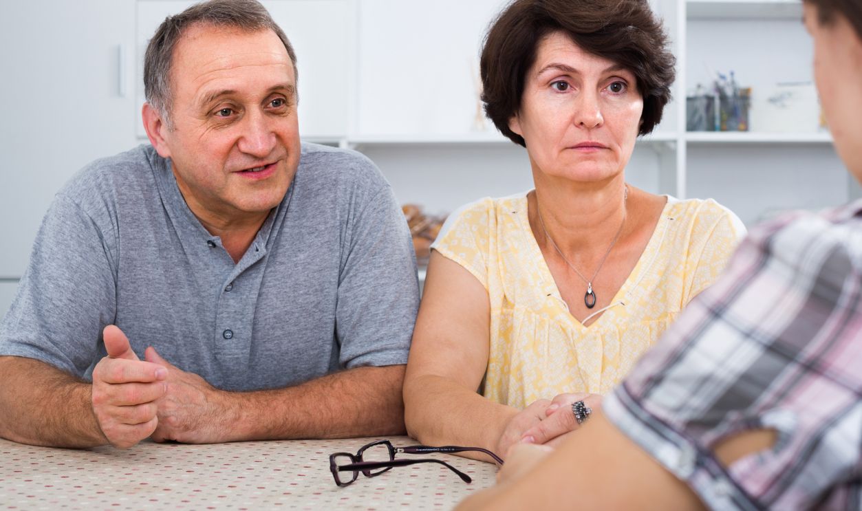 elderly parents attentively listening and talking to adult daughter at the table at home