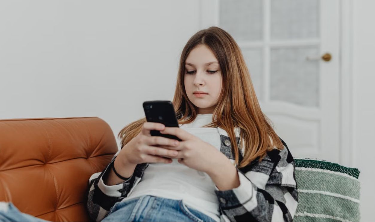 Teenage girl using smartphone while lounging on a sofa indoors.