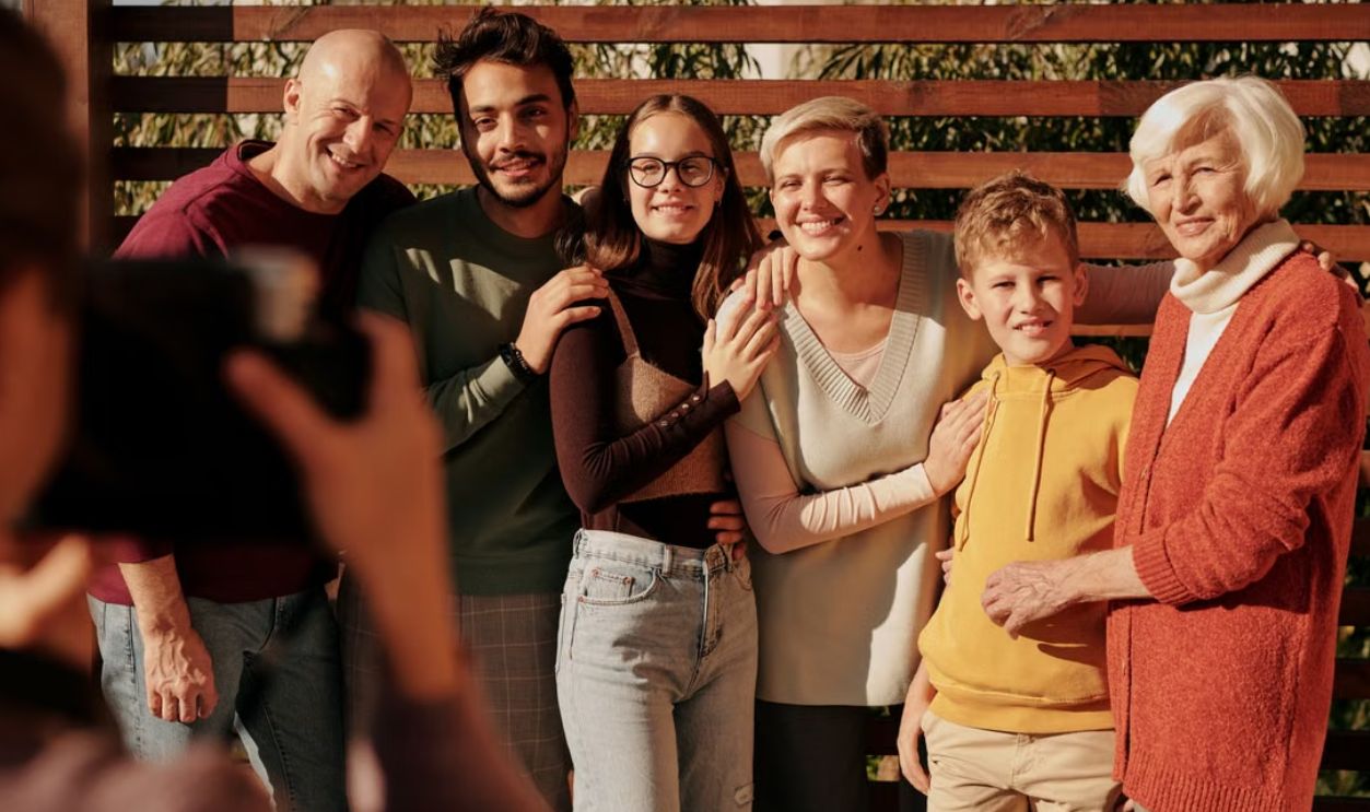 A joyful family portrait featuring multiple generations smiling outdoors in daylight