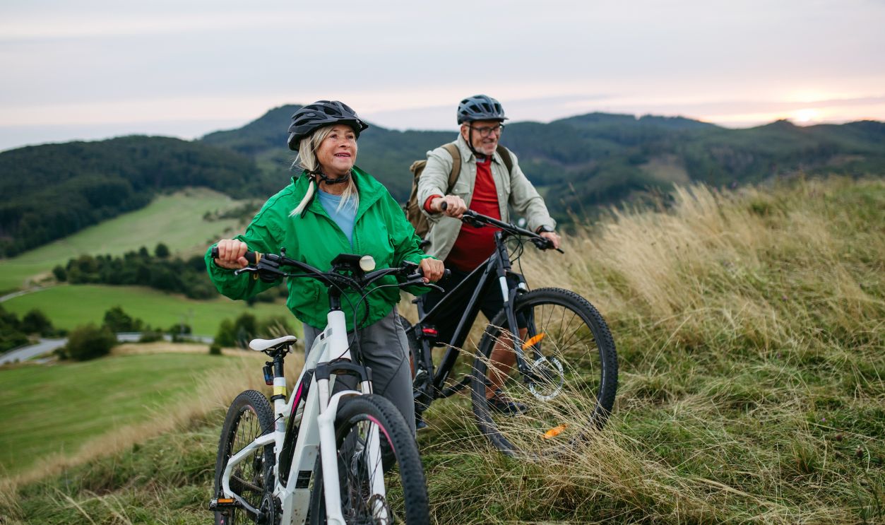 Older couple cycling together in nature, smiling and enjoying outdoor adventure.