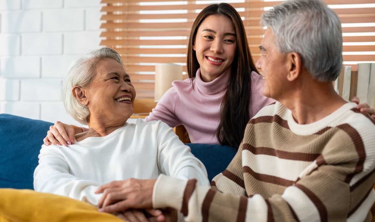 Asian lovely family, young daughter talking and sit with senior parent. Attractive woman granddaughter visit elder old mature couple in house enjoy spend leisure time together in living room and smile