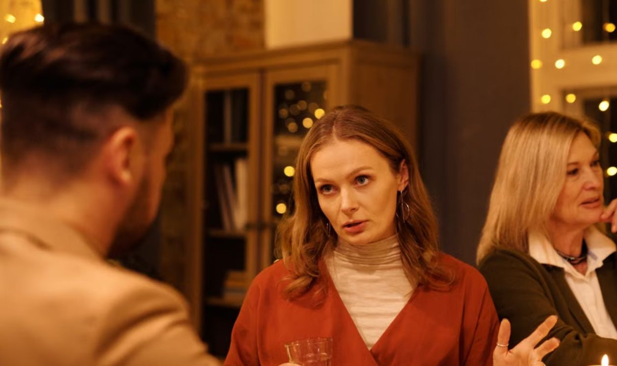 Three people enjoying a festive dinner table conversation surrounded by warm holiday lights.