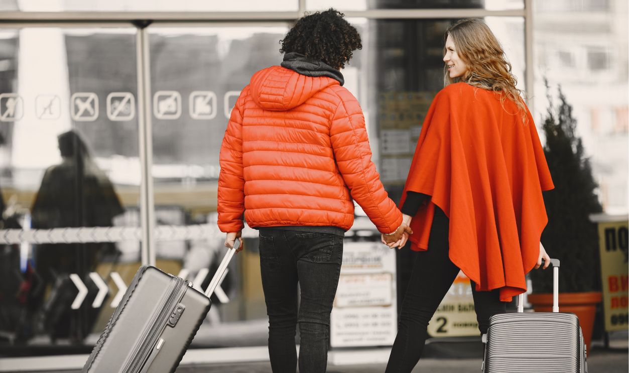 A couple holding hands with luggage, entering an airport for a travel